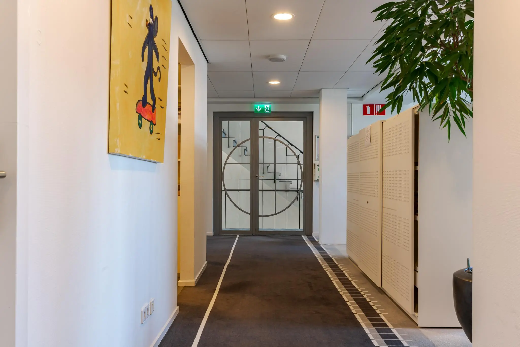 Modern kantoorinterieur aan de Van Alkemadelaan met kunst aan de muur en zicht op een deur naar het trappenhuis.